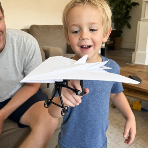 The RC Paper Airplane power module clipped to a folded paper plane beside its remote